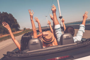 47807283 - enjoying road trip. rear view of young happy people enjoying road trip in their convertible and raising their arms up