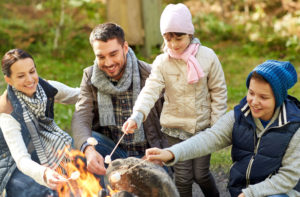 51496344 - camping, travel, tourism, hike and people concept - happy family roasting marshmallow over campfire
